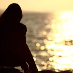 Woman sitting on rock overlooking body of water