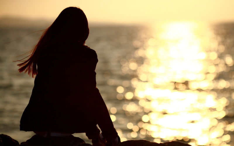 Woman sitting on rock overlooking body of water